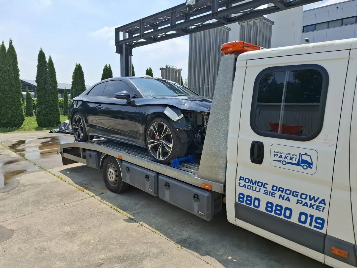 Czarne Audi z rozbitym przodem na lawecie na placu przemysłowym
