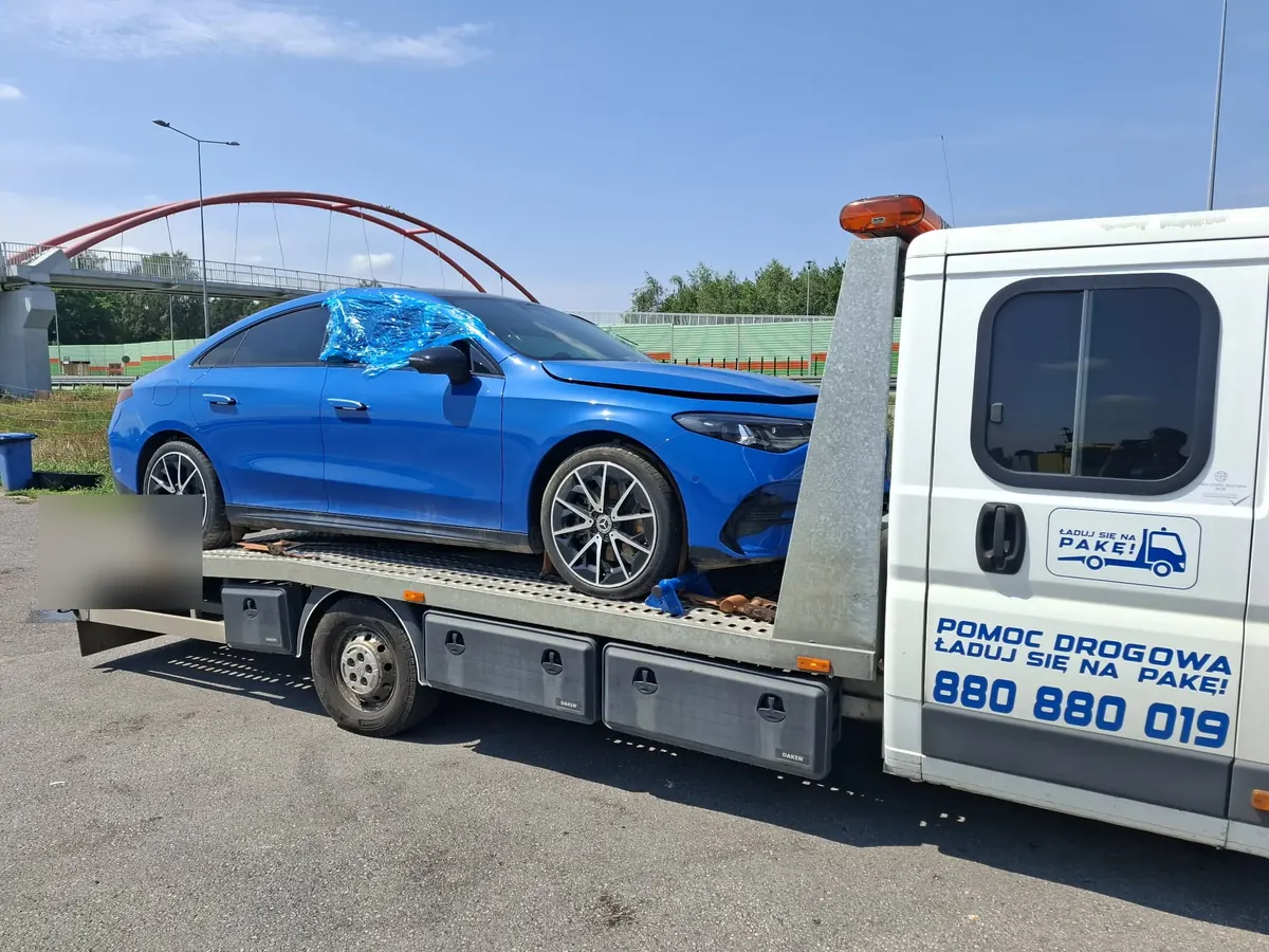 Niebieskie BMW po kolizji przodu, zabezpieczone folią, na platformie lawety