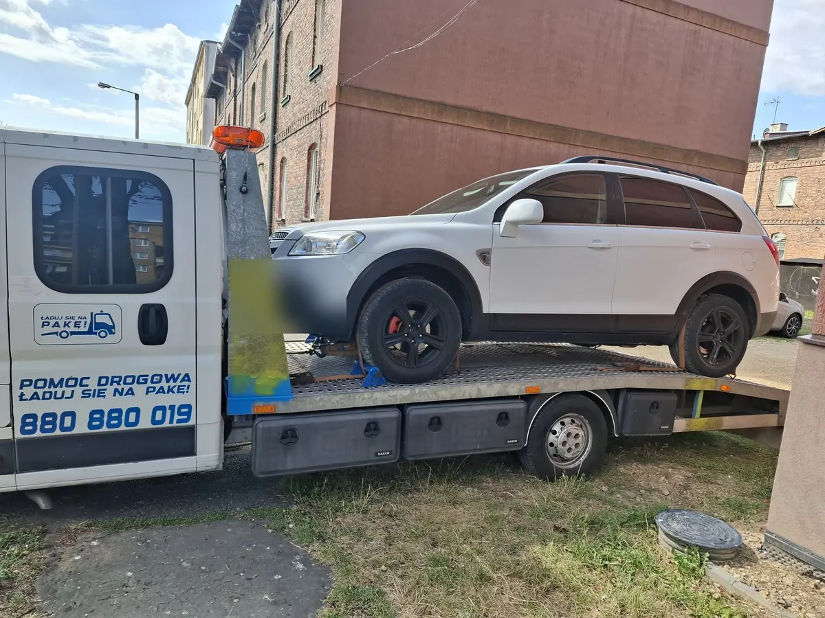 Biały Chevrolet Captiva na lawecie przy kamienicy