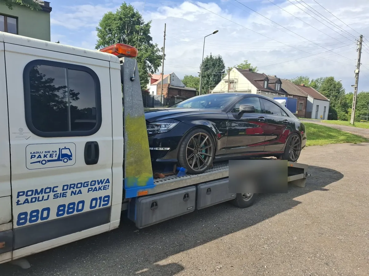 Czarny Mercedes kombi na platformie lawety na osiedlu