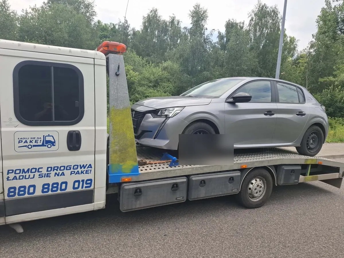 Szary Peugeot 208 na platformie lawety przy ulicy