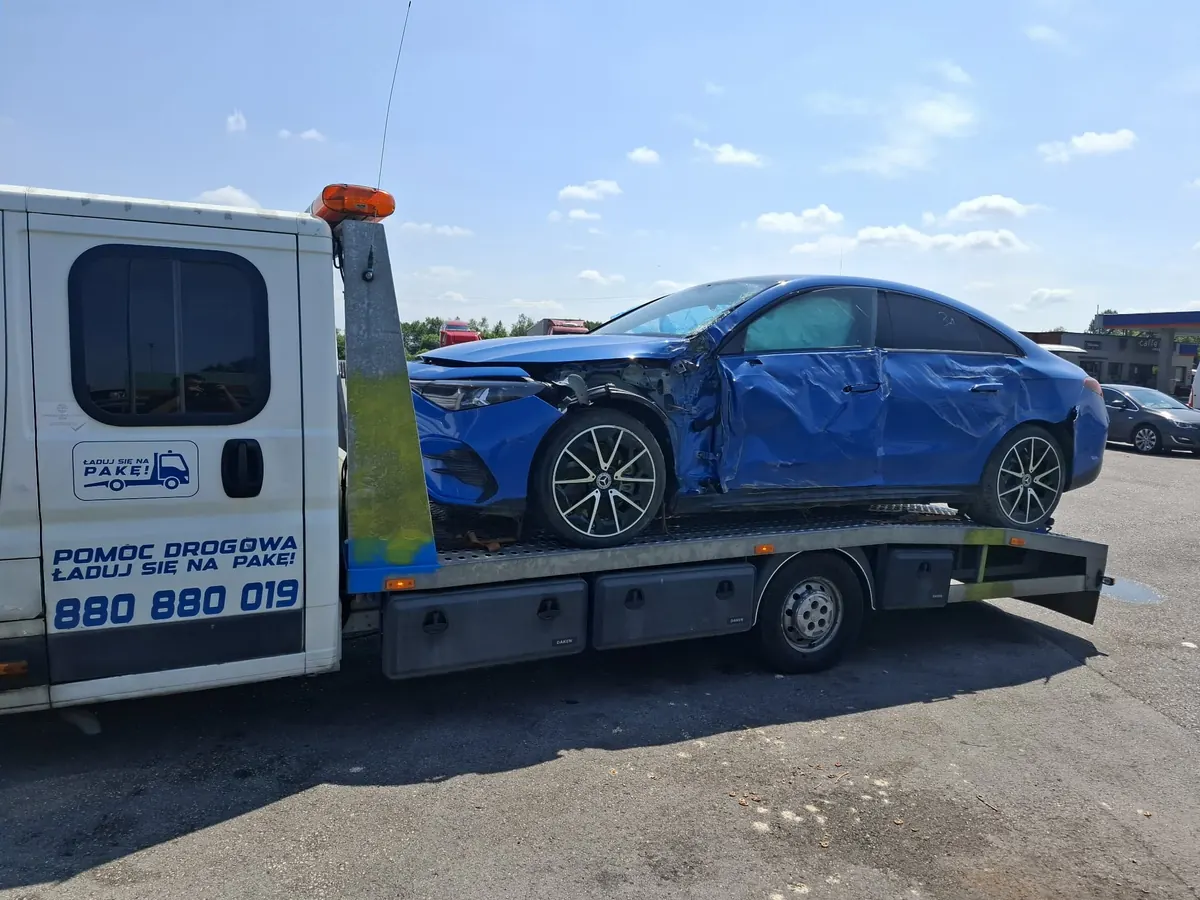 Niebieski sedan z wgniecionym bokiem po kolizji na platformie lawety